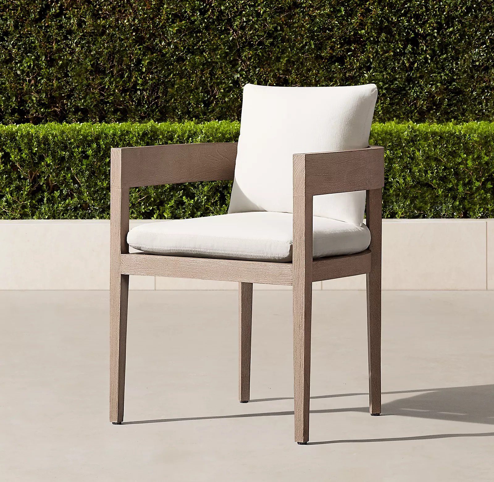 Teak long-legged outdoor dining chair with rounded back and armrest frame and white cushions