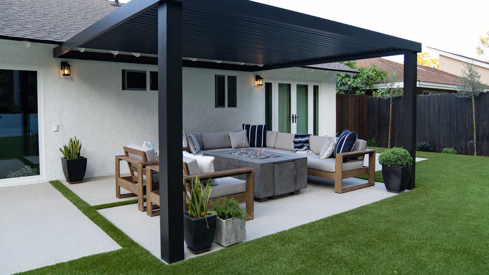 Black modern pergola attached to back of home over concrete paver patio and fire pit seating area