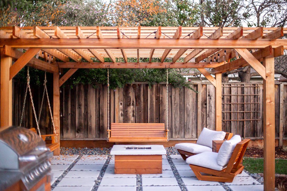 fire pit seating area with two lounge chairs and two bench swings suspended form a wooden pergola
