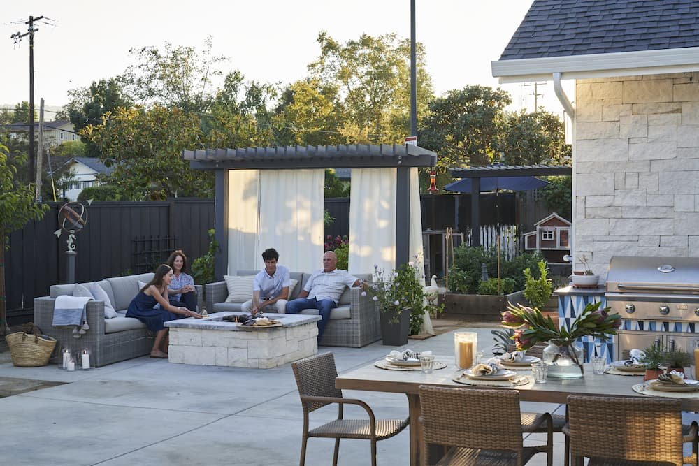family sitting around outdoor fire pit with cantilever pergola and shade curtain behind, and dining area in the foreground
