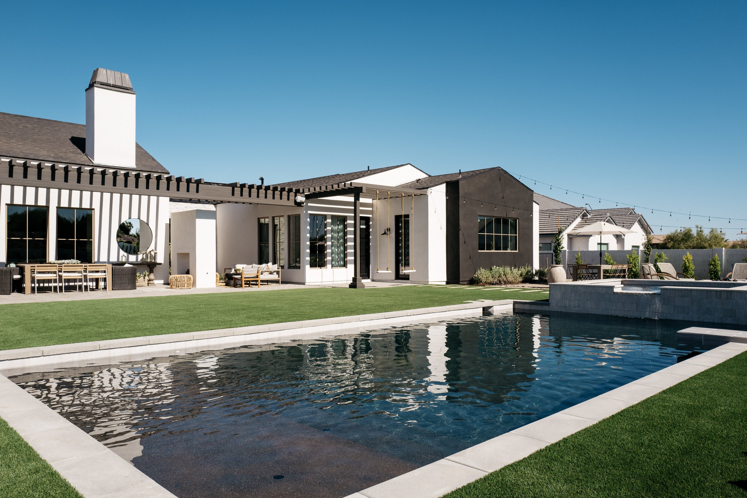 angled view of modern backyard with large pool, turf, and custom black pergola extending off back of home exterior