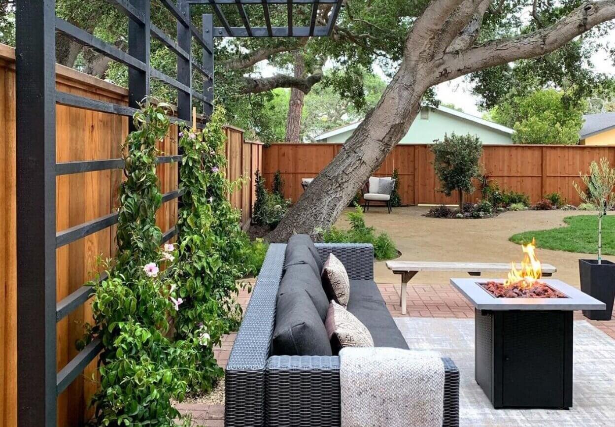 fire pit seating area with black cantilever pergola behind where plants are beginning to climb