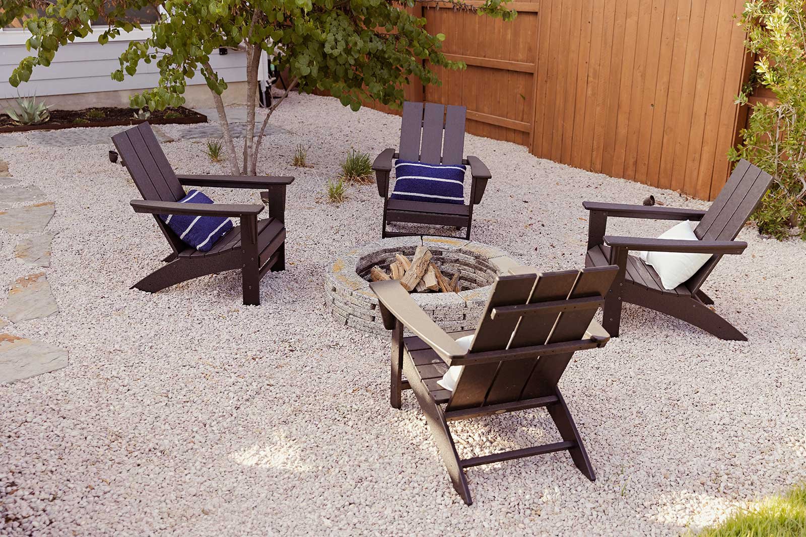 Crunchy gravel, comfy chairs, and an understory tree make for a cozy, rustic fire pit area. The zone adds value by offering a distinct experience from other gathering spaces in the yard.